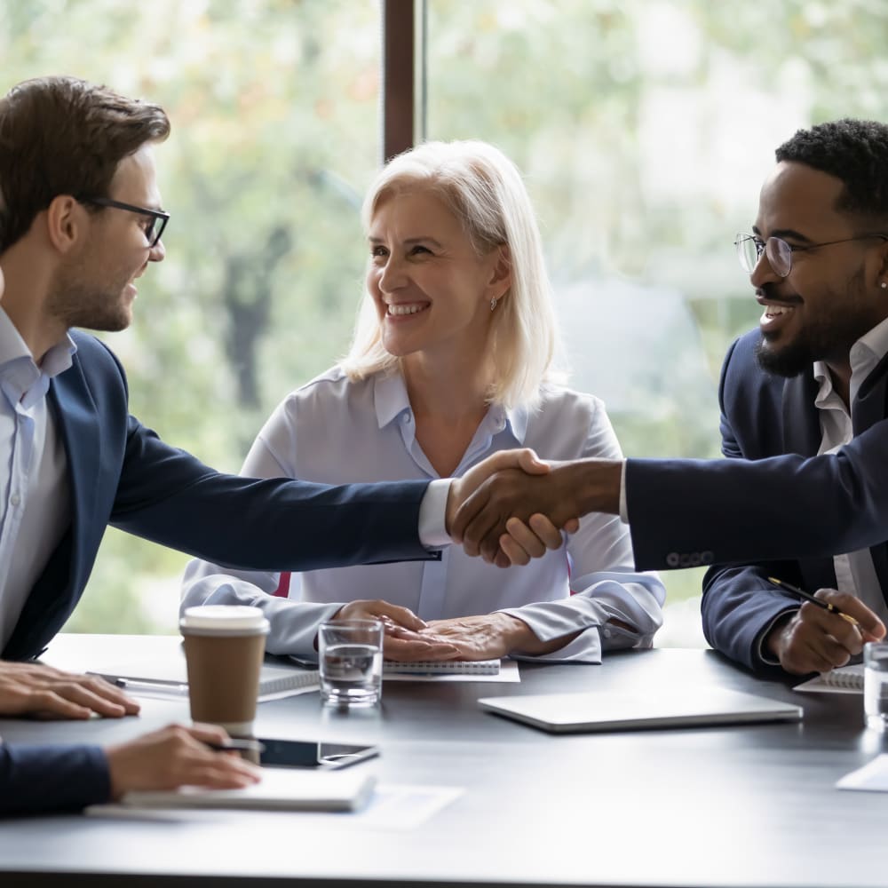 A group of three business people are sitting at a table smiling.