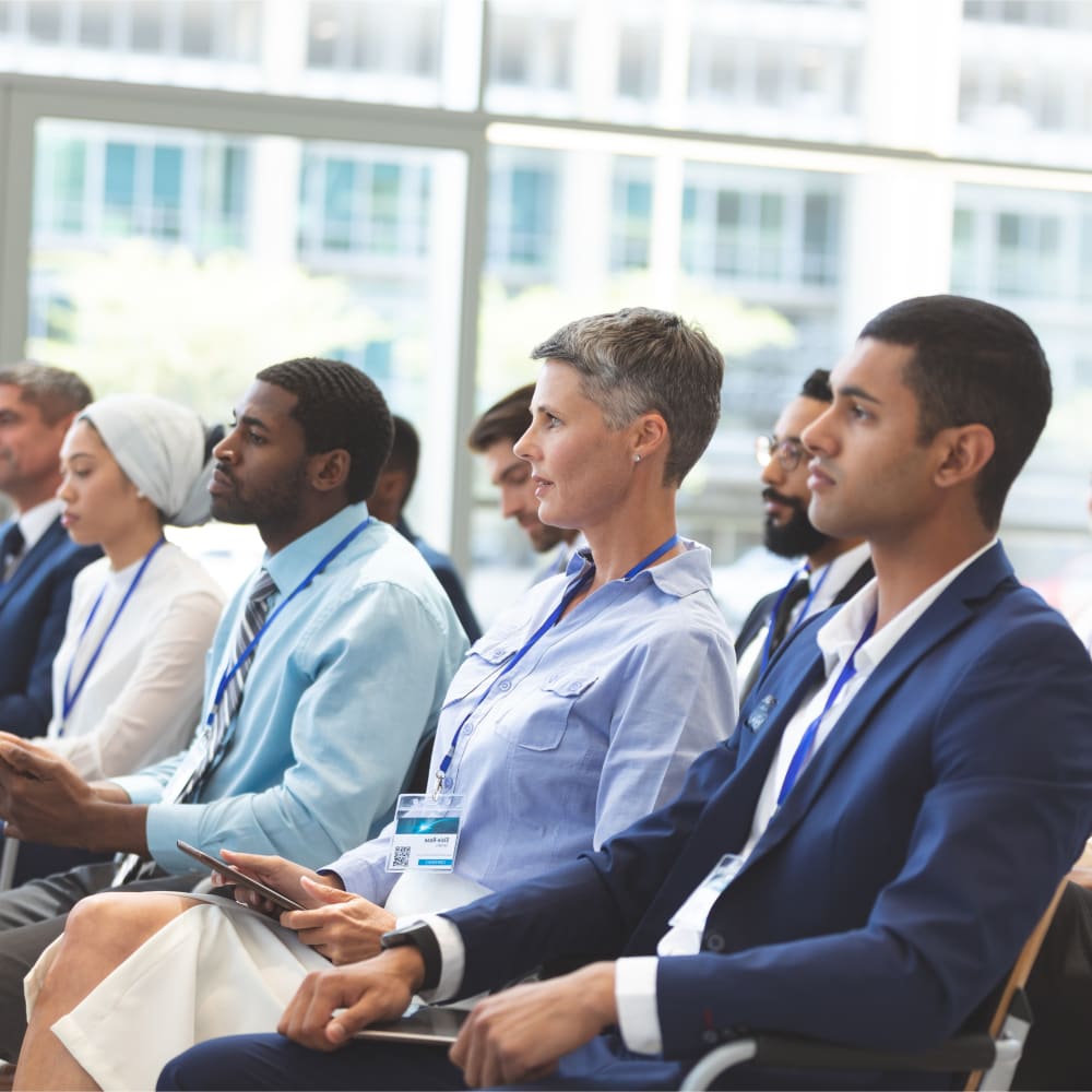 A group of professionals are sitting in a row, like they are an audience spectating an event.